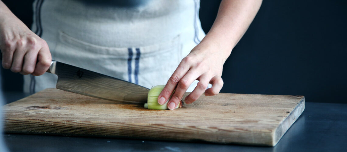 person using a knife to cut an onion on a cutting board
