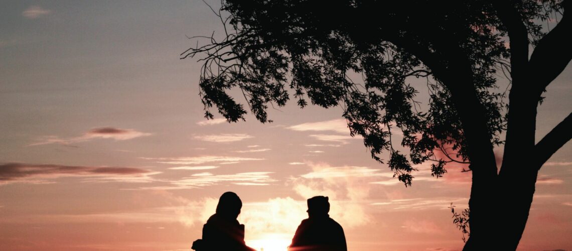 Couple sitting outside under a tree with the sunset